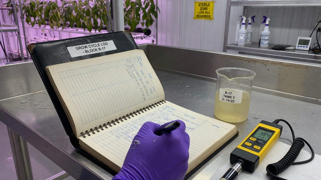 Hand in a glove that writes in a logbook on a stainless steel bench near an EC meter